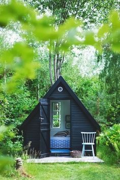 a small black cabin in the woods with a blue bed and white chair on it