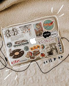 an apple laptop covered in stickers on top of a bed