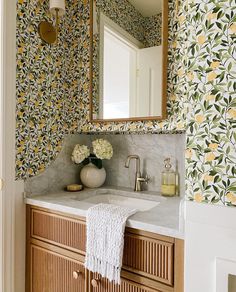 a bathroom with floral wallpaper and marble counter top, gold faucet, white towel on wooden cabinet