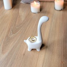 a white cat shaped candle holder sitting on top of a wooden table next to candles