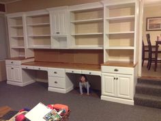 a child sitting in the corner of a room under a desk with drawers and shelves