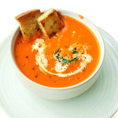 a bowl of tomato soup with bread on the side and garnished in parmesan cheese