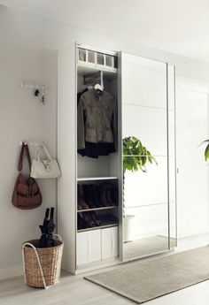 an open closet with clothes hanging on the door and a basket in front of it