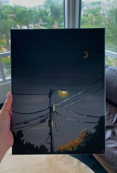 a person holding up an image of the moon and power lines in front of them