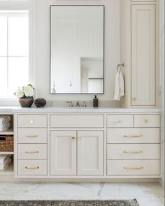 a bathroom with white cabinets and gold pulls on the mirror above the sink is an area rug