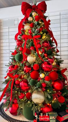 a christmas tree decorated with red and gold balls, ornaments and bows is on display