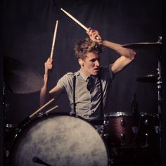 a young man playing drums in front of a drum set with his hands behind him