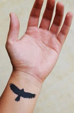 a hand with a black bird tattoo on it's left arm and the wrist