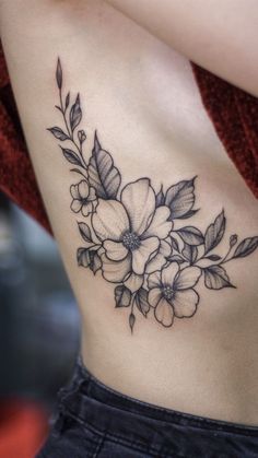 a woman's stomach with flowers and leaves tattooed on her side ribcage