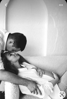 a man kissing a woman on the cheek while sitting in front of a couch with his arm around her