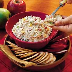 a person holding a spoon in a red bowl filled with coleslaw and crackers