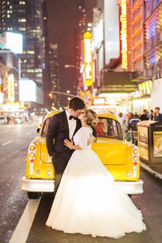 a bride and groom kissing in front of a taxi cab on the street at night