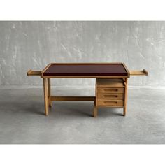 a desk with two drawers and a brown leather top on the bottom, in front of a concrete wall