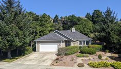 a house with lots of trees in front of it and a car parked on the driveway