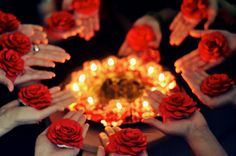 many hands holding roses in front of a lit candle