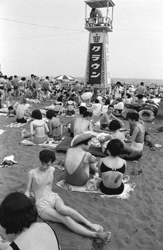 many people are sitting on the beach and one person is standing in front of a light house