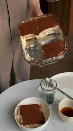 someone is holding up a cake in front of the plate with two bowls on it