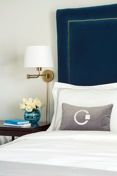 a bed with blue headboard and white linens on it, next to a night stand