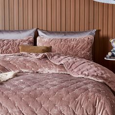 a bed with pink comforter and pillows on top of it next to a night stand