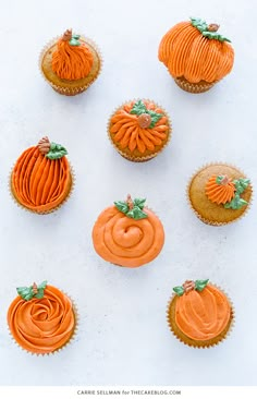 several cupcakes with frosting and pumpkin decorations on white paper, top view