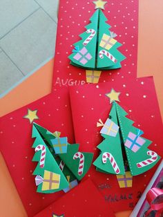 three christmas trees made out of paper on top of red envelopes with gold stars and candy canes