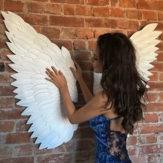 a woman in a blue dress with white wings on her face and arms, leaning against a brick wall