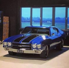 a blue and black muscle car parked in a garage with large windows overlooking the water