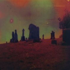 a group of tombstones sitting on top of a grass covered hill under a colorful sky