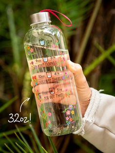 a person holding up a water bottle with writing on it and flowers in the bottom