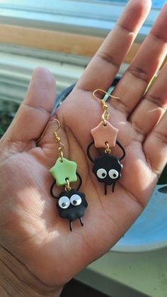 the hand is holding three small earrings with googly eyes and stars on them,