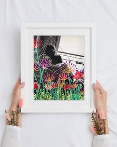 two hands holding up a framed photograph with flowers in the foreground and a piano in the background