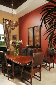 a dining room table and chairs in front of a red wall with palm leaves on it