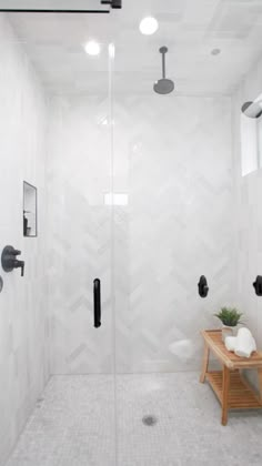 a walk in shower sitting next to a white tiled wall and wooden bench with potted plant on it