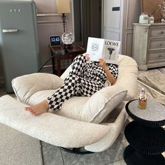 a woman laying on top of a white chair holding a book in her hands and reading it