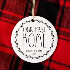 a white ornament hanging from a red and black checkered blanket with the words our first home on it