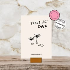 a card that says table one with two glasses of wine and a pink rose on it