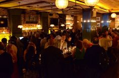 a large group of people sitting at tables in a room with lights on the ceiling