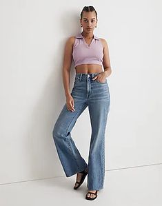 a woman leaning against a wall with her hands on her hips wearing high rise jeans