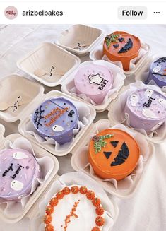 there are many decorated cupcakes in plastic containers on the table with white cloth