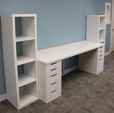 a white desk and bookcases in an empty room with light blue wall paint