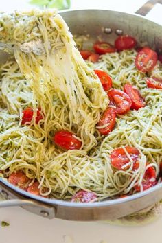 the pasta is being stirred with a wooden spatula and garnished with tomatoes