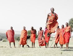 a group of men standing around each other in front of a field with trees and bushes