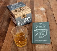 a glass of whiskey next to a book on a wooden table