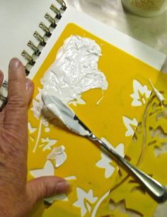 a person is painting with white paint on a yellow piece of paper and silver scissors