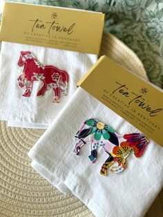 two tea towels with colorful horses on them sitting on a table next to a box