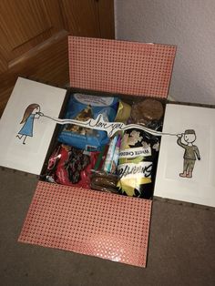 an open gift box filled with treats and candys on top of a table next to two pictures