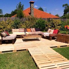 a wooden deck with couches and tables in the grass near a fenced area