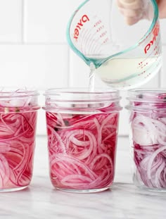 a person pouring dressing into jars filled with red onions