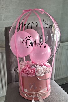 a birthday card with balloons and flowers in a pink hat box on a gray chair