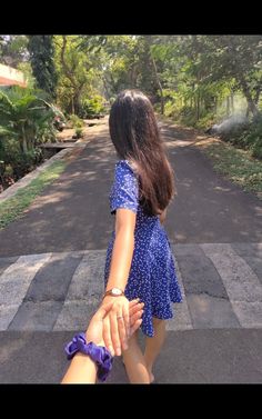 two people holding hands while walking down the street in front of some trees and bushes